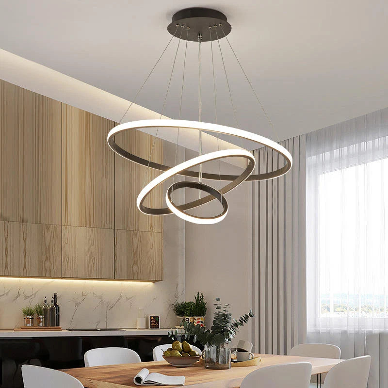 Modern three-ring LED ceiling light suspended above a wooden dining table in a contemporary kitchen, featuring a sleek, minimalist circular design.