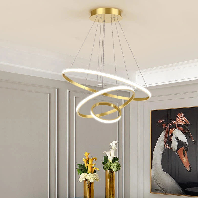 Modern gold three-ring LED ceiling light suspended in a stylish living room with elegant wall panelling and floral decor.