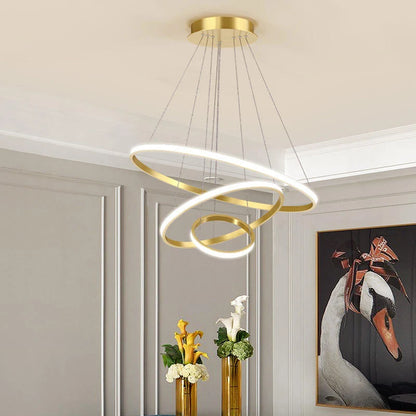 Modern gold three-ring LED ceiling light suspended in a stylish living room with elegant wall panelling and floral decor.