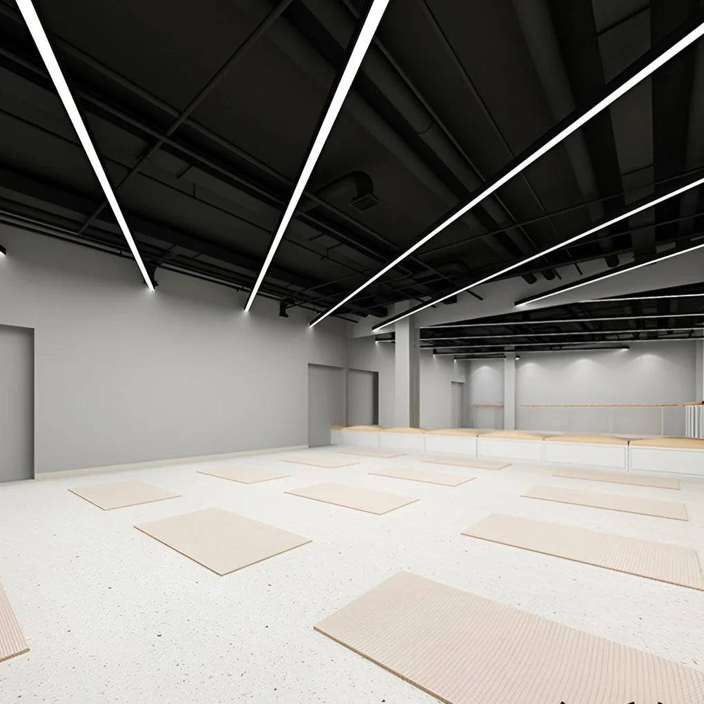 Modern black linear LED pendant lights installed on a dark industrial ceiling in a bright, minimalist yoga studio with light-coloured floor mats.