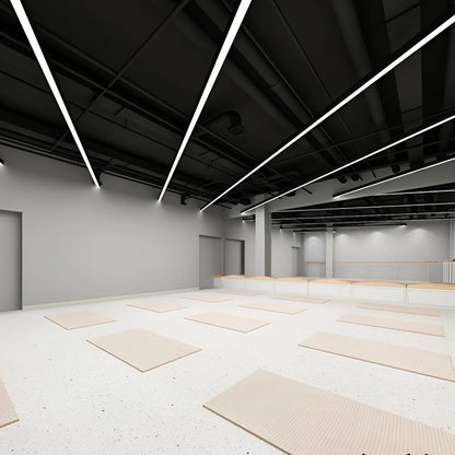 Modern black linear LED pendant lights installed on a dark industrial ceiling in a bright, minimalist yoga studio with light-coloured floor mats.