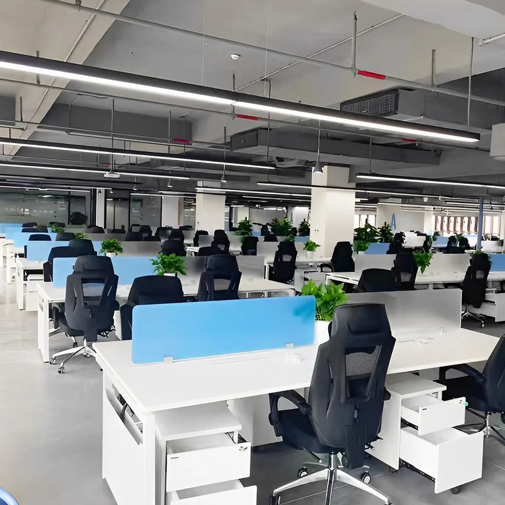 Modern black linear LED pendant lights suspended from an industrial ceiling in a bright, open-plan office space with white desks and black chairs.