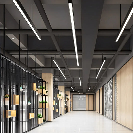 Modern black linear LED pendant lights suspended from a dark industrial ceiling in a contemporary commercial office corridor with wooden accents.