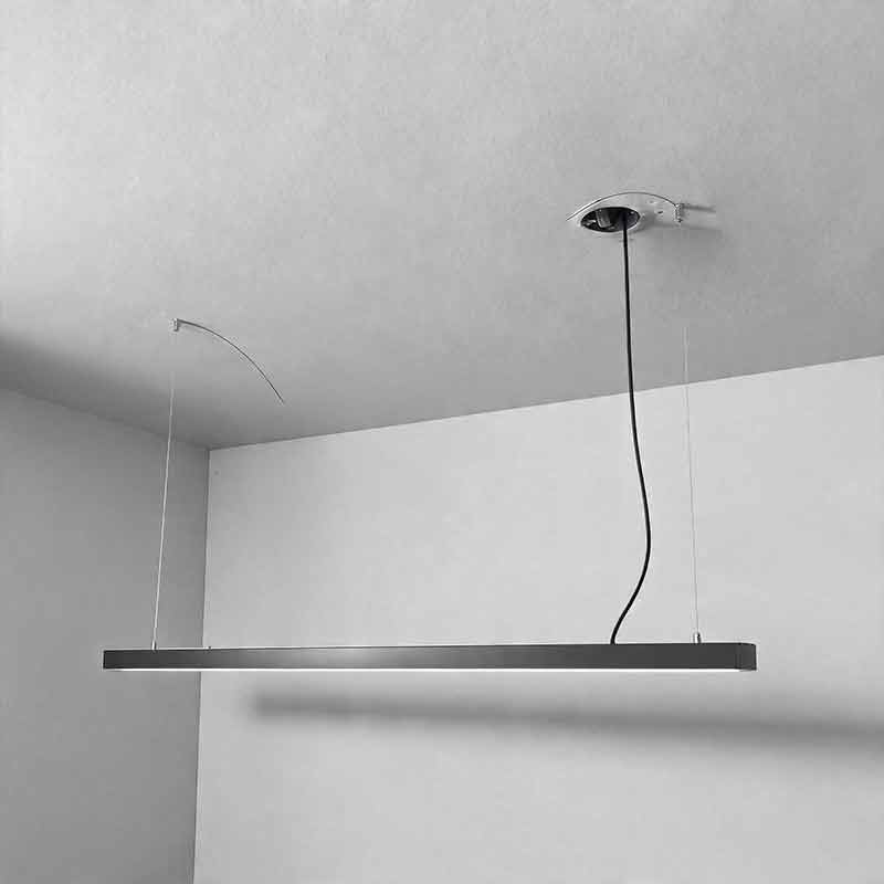 A sleek black linear LED pendant light suspended from a ceiling by thin wires, providing modern minimalist lighting for a commercial office space.