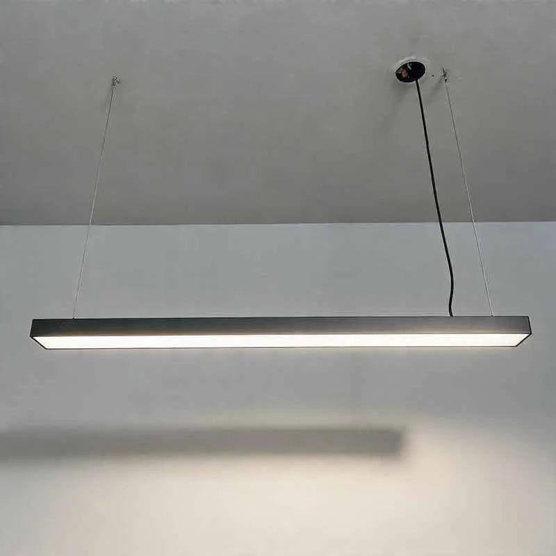 A sleek black linear LED pendant light suspended from a ceiling by thin wires, providing modern illumination for a commercial or office workspace.