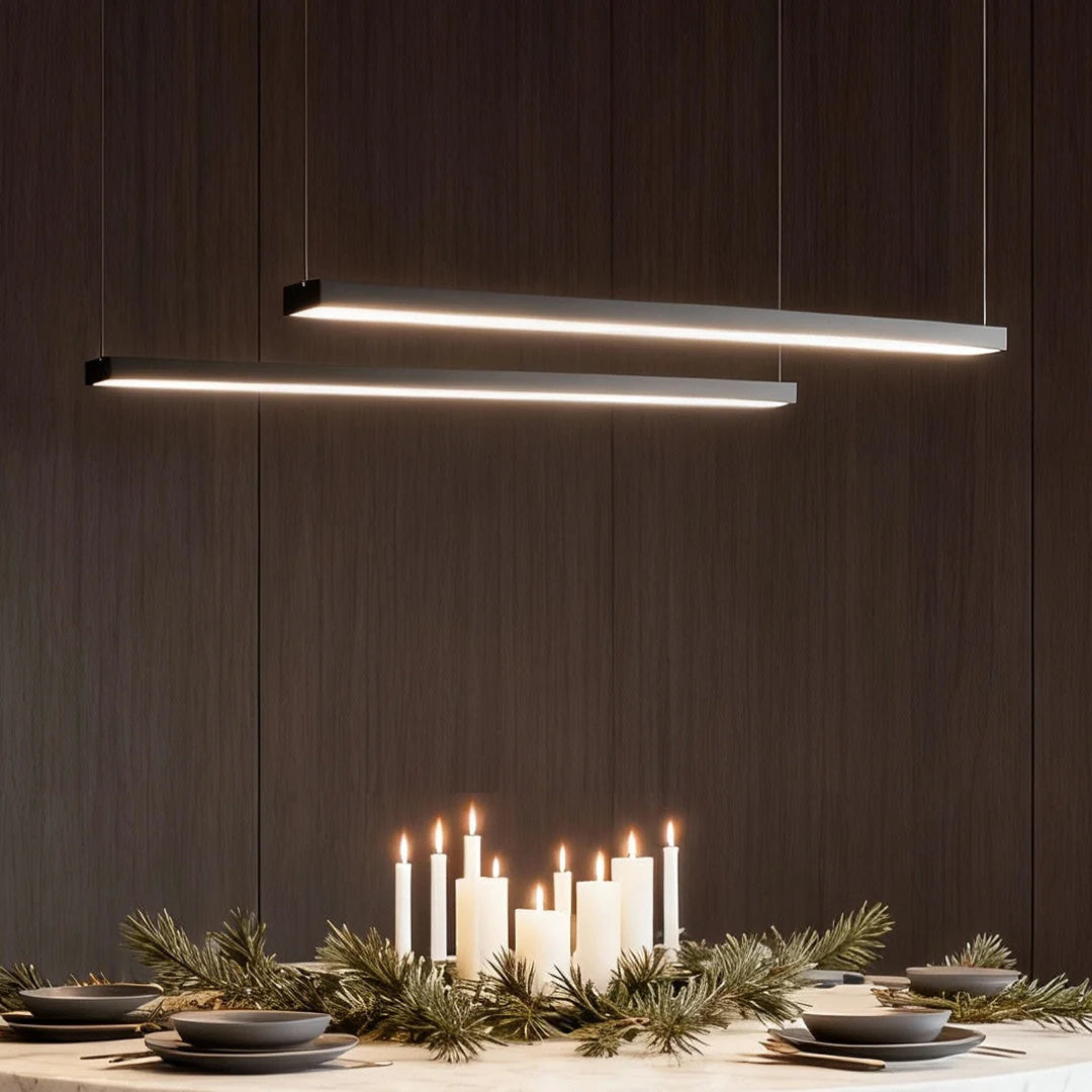 Two modern black linear LED pendant lights suspended above a dining table decorated with candles and pine branches for a festive commercial setting.