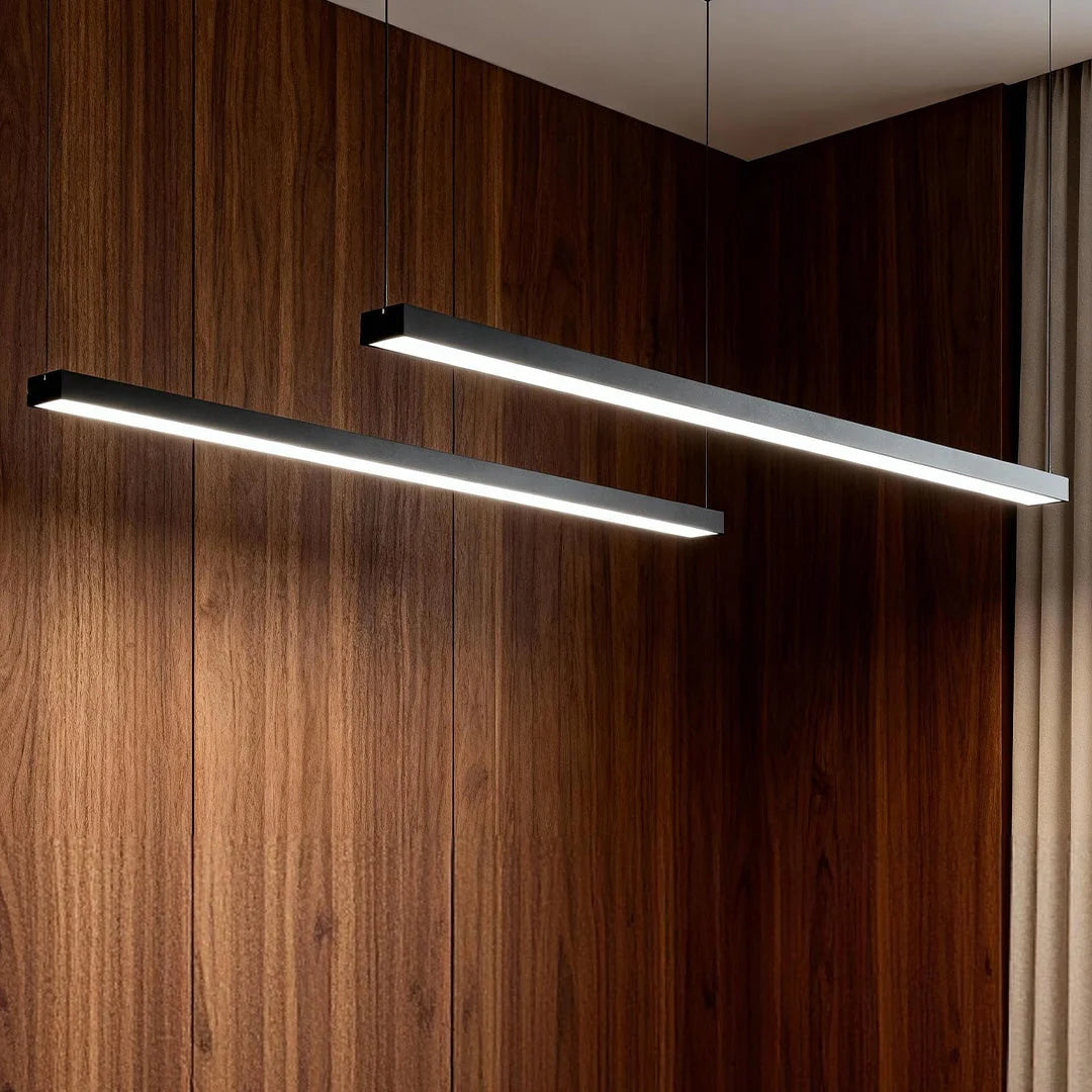 Two modern black linear LED pendant lights suspended against a dark wood panelled wall, providing sleek, minimalist illumination for commercial spaces.