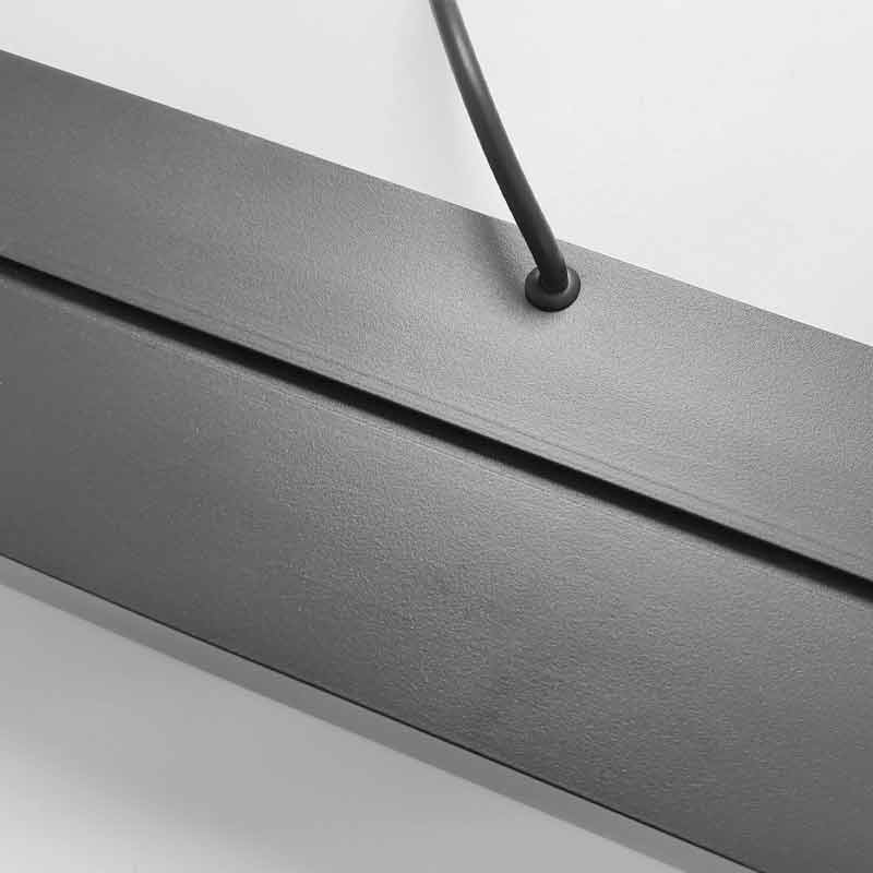 Close-up of a matte black linear LED pendant light fixture showing the textured finish and the power cable attachment point for commercial interiors.