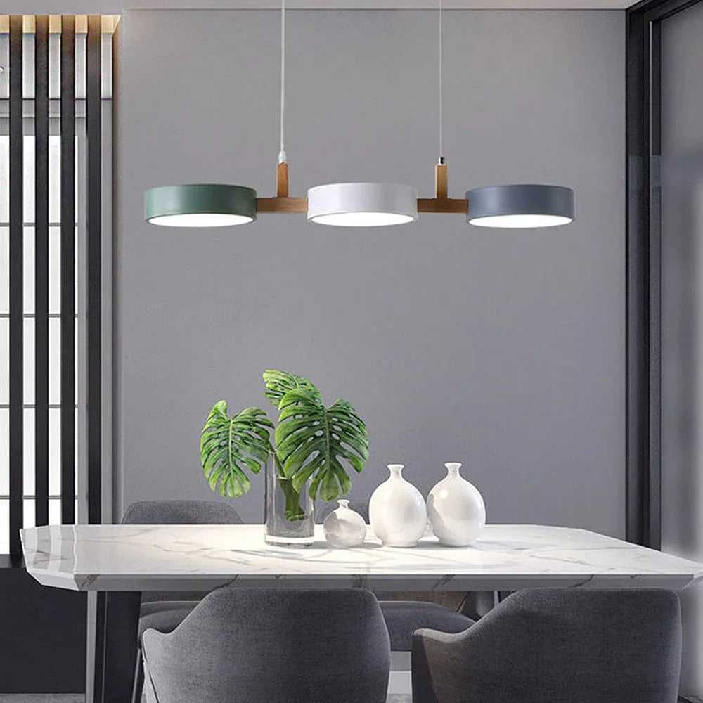 Modern 3-light pendant with green, white and grey circular shades and wood accents hanging above a marble dining table in a contemporary room.