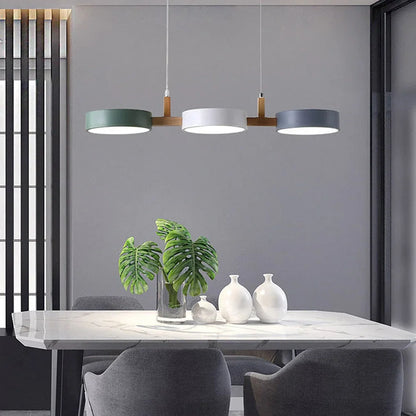 Modern 3-light pendant with green, white and grey circular shades and wood accents hanging above a marble dining table in a contemporary room.