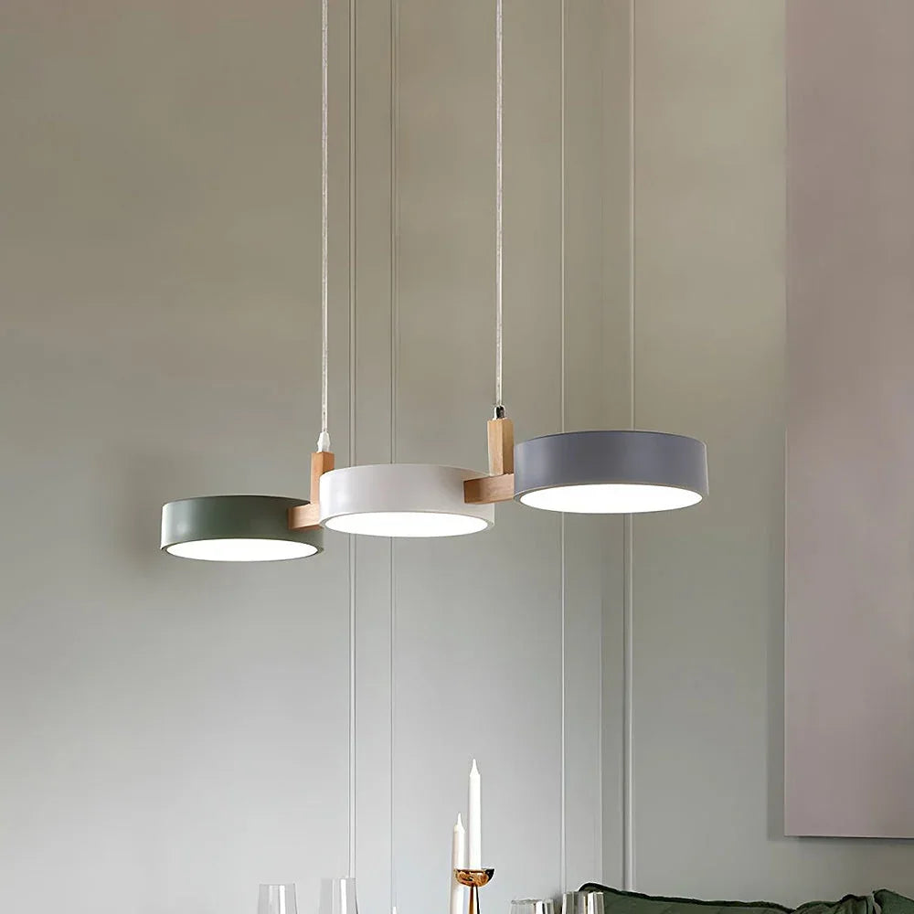 Modern sculptural 3-light pendant featuring three circular shades in green, white and grey, connected by light wood accents, hanging in a dining room.