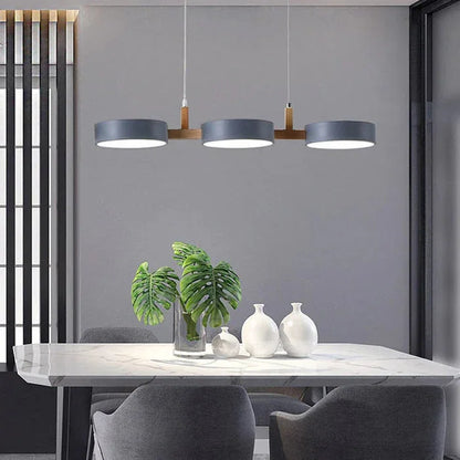 Modern 3-light pendant featuring grey circular shades and wood accents hanging above a marble dining table in a contemporary kitchen setting.