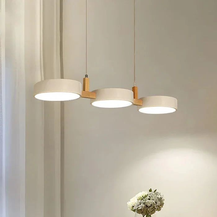 Modern white 3-light pendant with natural wood accents, featuring three circular illuminated discs suspended above a dining area in a contemporary home.