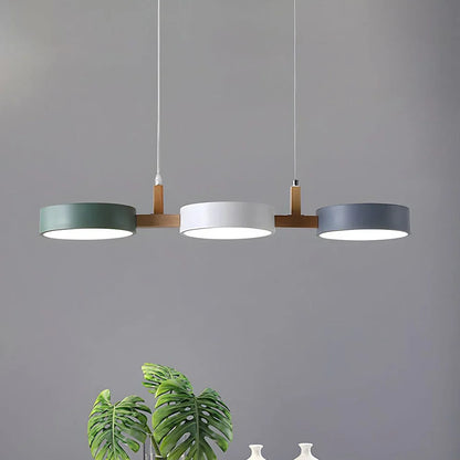 Modern 3-light pendant featuring green, white and grey circular shades with natural wood accents, suspended above a dining area with a houseplant.