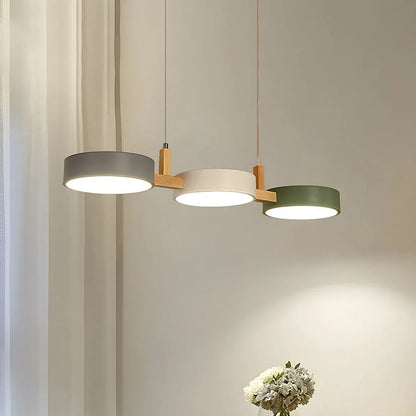 Modern 3-light pendant featuring grey, white, and green circular shades with natural wood accents, emitting a warm glow in a contemporary dining room.