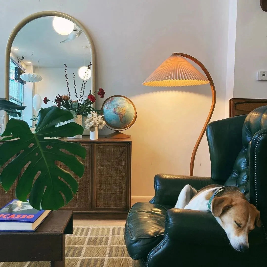 Nordic beech wood floor lamp with a pleated shade illuminating a cosy living room corner featuring a green leather armchair and a sleeping dog.