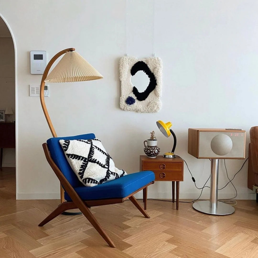 Nordic beech wood floor lamp with a pleated shade positioned next to a vibrant blue armchair in a modern living room with parquet flooring.