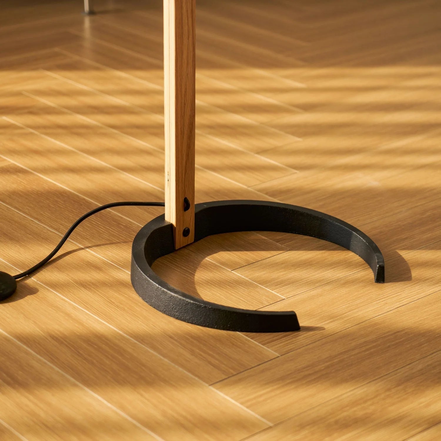 Close-up of the Nordic beech wood floor lamp base, featuring a sturdy black circular stand resting on a light wooden floor with warm sunlight shadows.