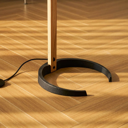Close-up of the Nordic beech wood floor lamp base, featuring a sturdy black circular stand resting on a light wooden floor with warm sunlight shadows.
