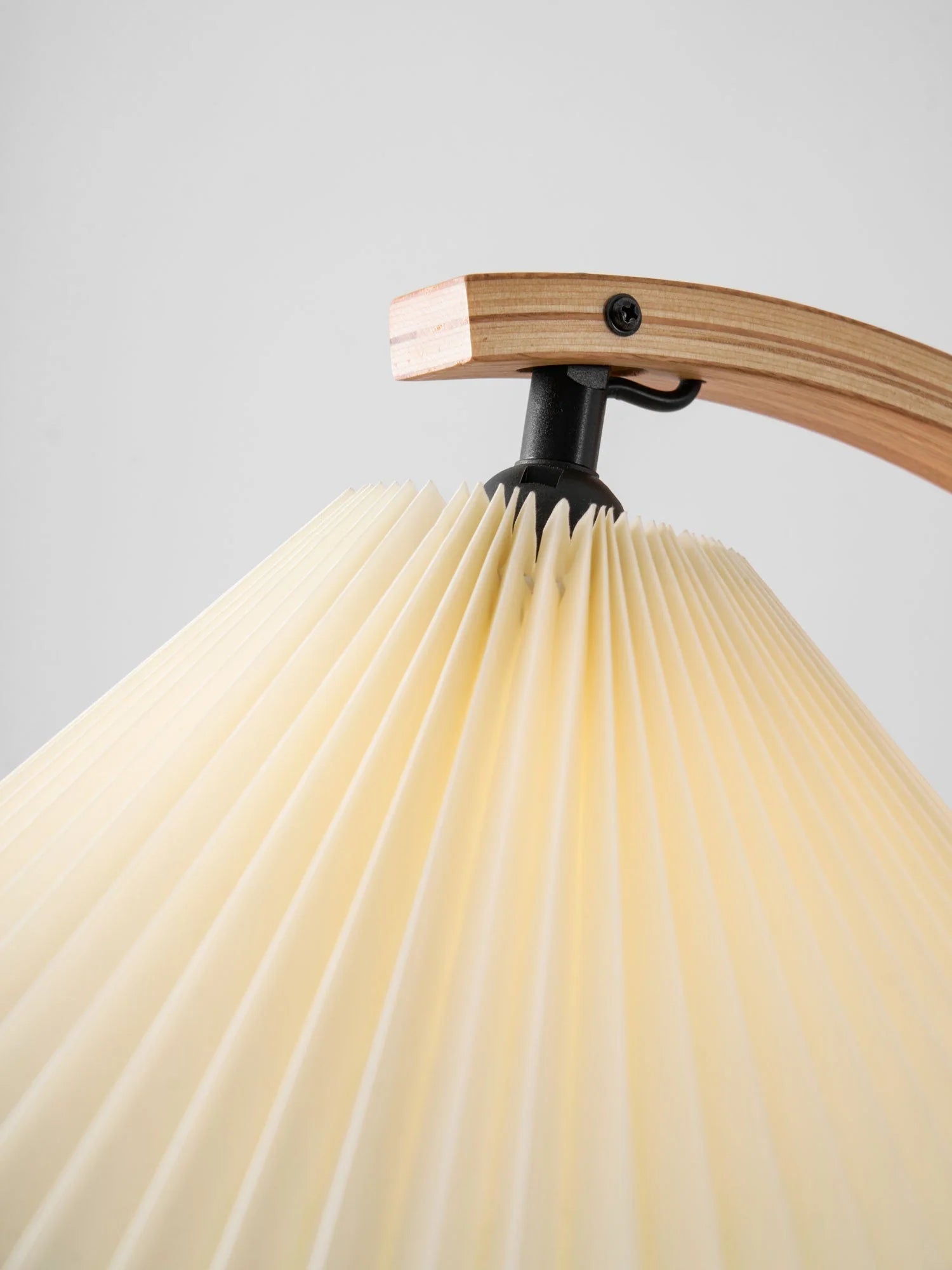 Close-up of the pleated cream lampshade attached to a curved Nordic beech wood arm on a modern floor lamp against a plain light background.