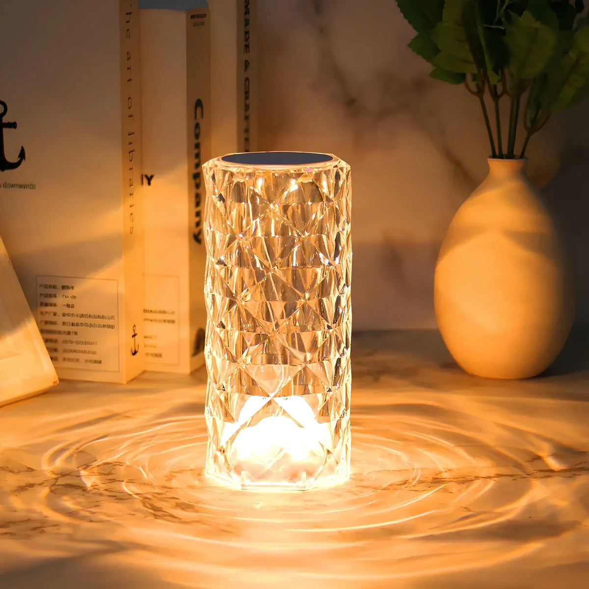 Crystal-effect table lamp glowing warmly beside books and a vase