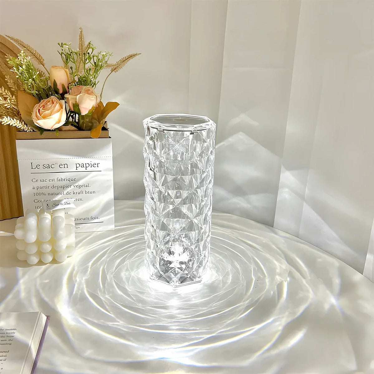Clear cylinder lamp casting white patterned light beside flowers