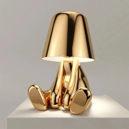 A modern, rechargeable gold figure table lamp with a minimalist design, featuring a seated character shape and a smooth, reflective metallic finish.
