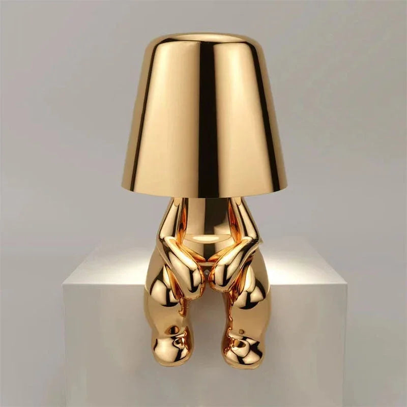 Modern gold rechargeable LED table lamp featuring a minimalist sitting figure design with a smooth metallic finish, perfect for a bedside or desk.