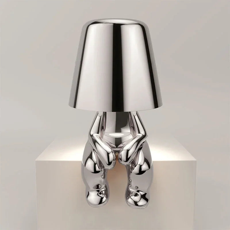 Modern silver rechargeable LED table lamp featuring a minimalist sitting figure design with a smooth metallic finish, perfect for a bedside or desk.