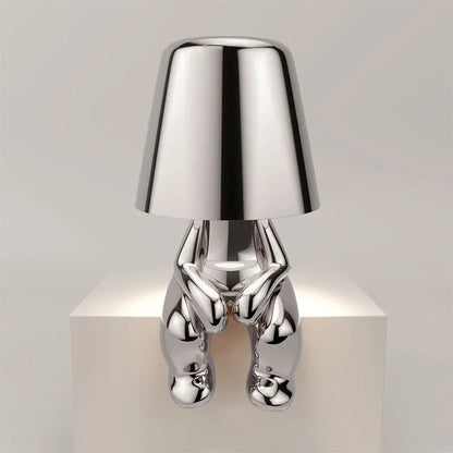 Modern silver rechargeable LED table lamp featuring a minimalist sitting figure design with a smooth metallic finish, perfect for a bedside or desk.