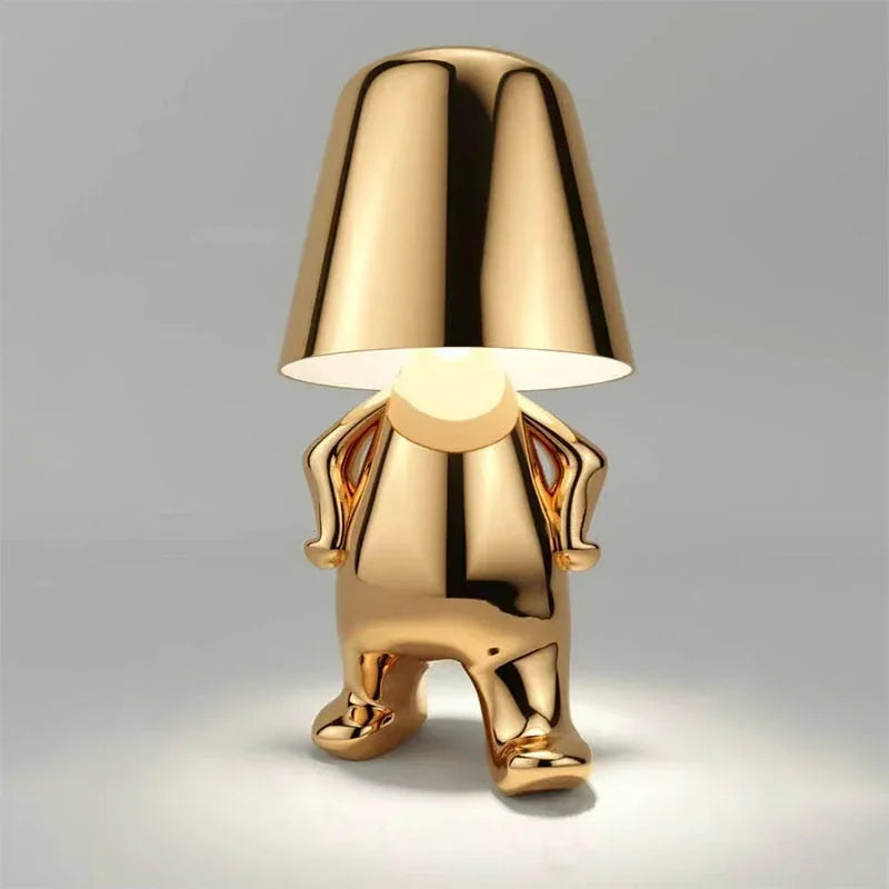 Gold rechargeable LED table lamp in a walking figure design with a minimalist metallic finish and touch control, perfect for a modern bedside.