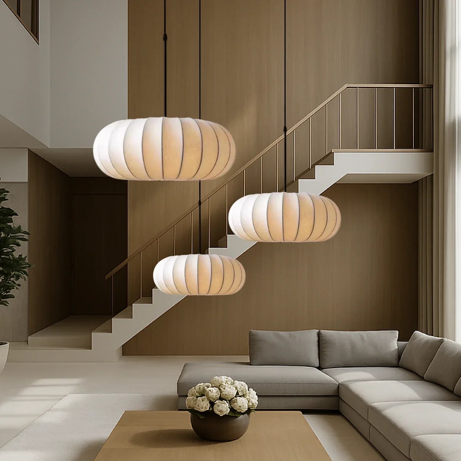 Three retro silk pumpkin pendant lights hanging at staggered heights in a modern living room featuring a neutral sofa, coffee table and staircase.