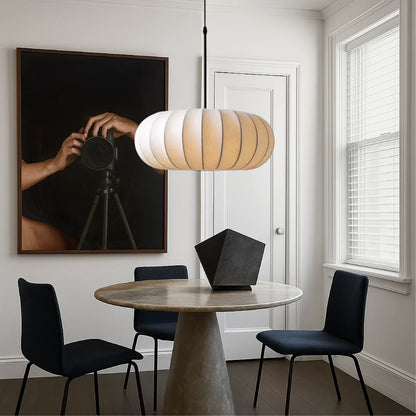 A retro silk pumpkin pendant light suspended above a round dining table with dark blue chairs in a stylish, modern dining room.