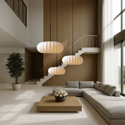 Three retro silk pumpkin pendant lights hanging at different heights in a modern, minimalist living room with a large sofa and wooden coffee table.