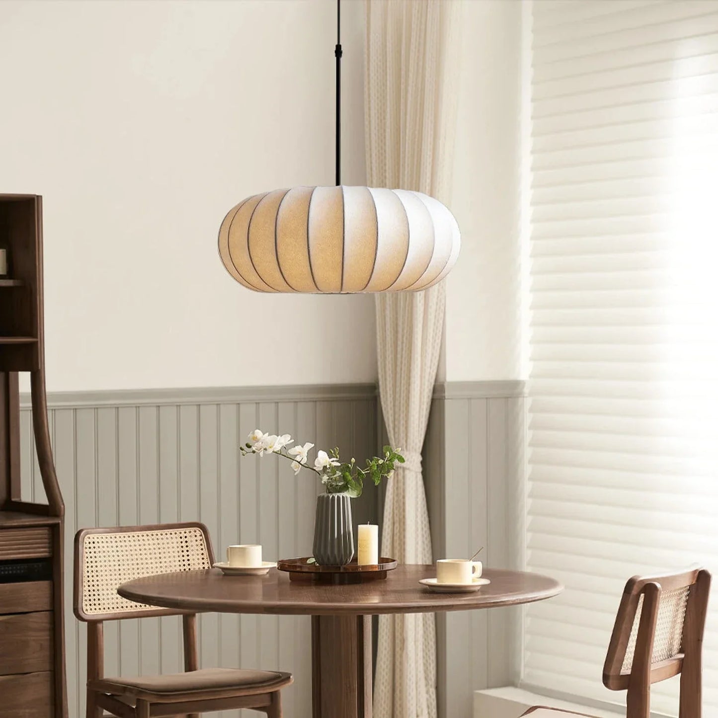 A retro pumpkin-shaped silk pendant light hanging above a round wooden dining table with chairs in a cosy, neutral-toned dining room.