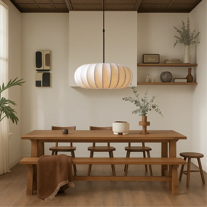 A retro silk pumpkin pendant light in cream hangs above a wooden dining table and bench in a warm, minimalist dining room setting.