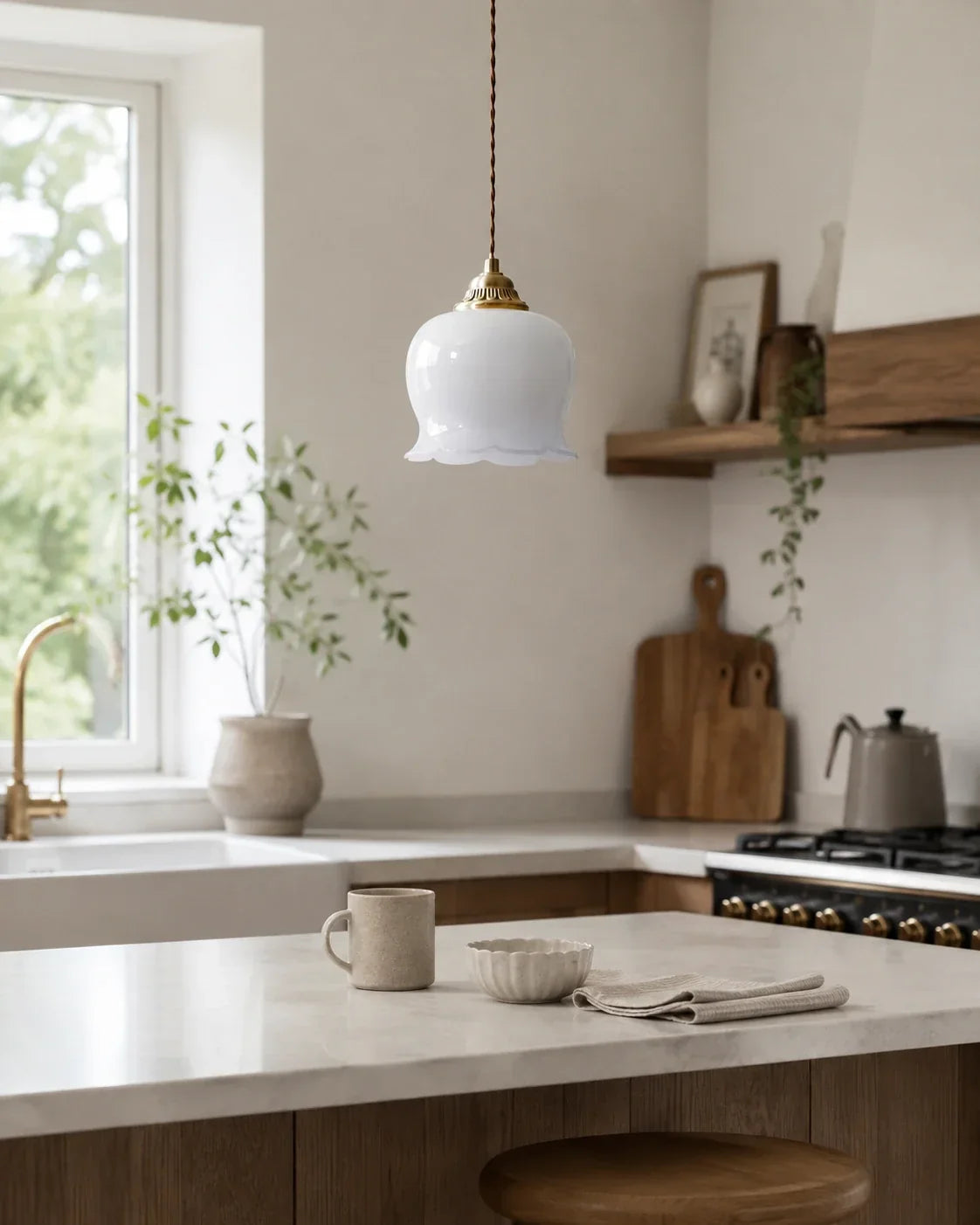 A white glass scalloped floral pendant light with brass details hanging above a kitchen island in a bright, rustic-style kitchen.