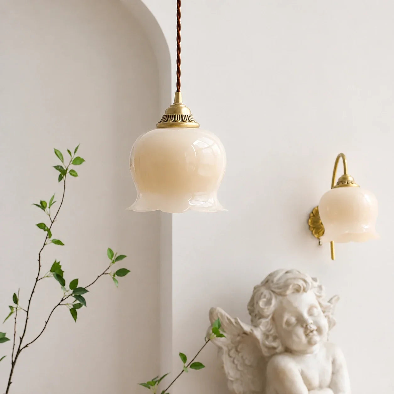 A vintage-style scalloped floral pendant light with a cream glass shade and brass fixture, hanging in a bright room with a matching wall light.