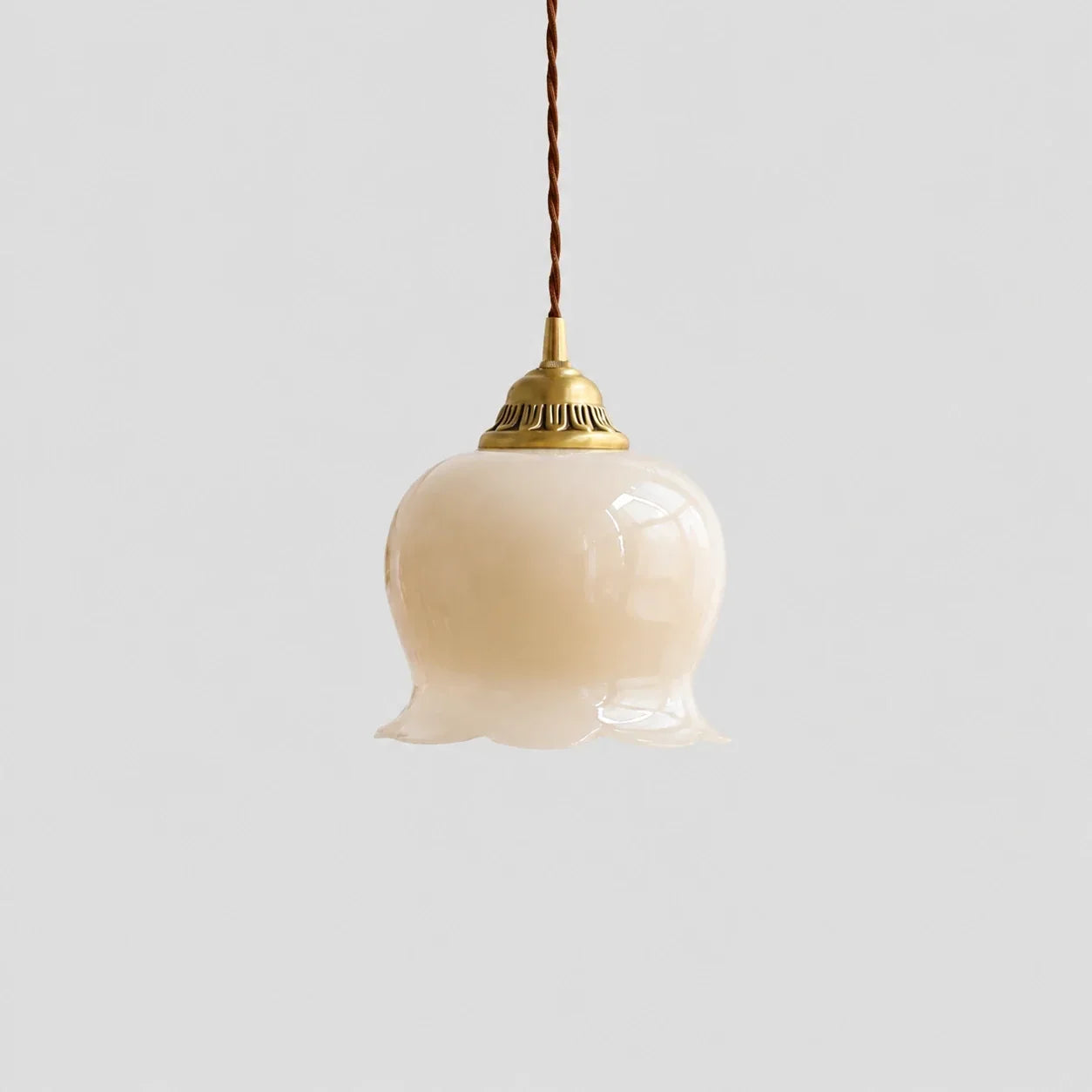 Scalloped Floral Pendant Light featuring a pale cream glass flower-shaped shade, brass fixture, and a brown braided cord against a plain background.