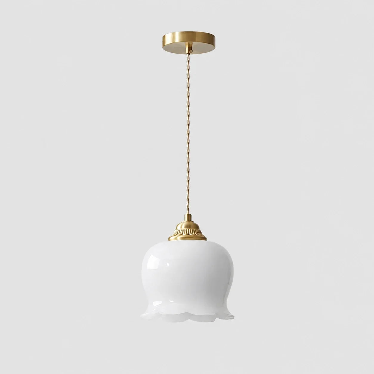 A white glass pendant light featuring a scalloped floral-shaped shade, suspended from a brass ceiling rose by a twisted gold-coloured cord.
