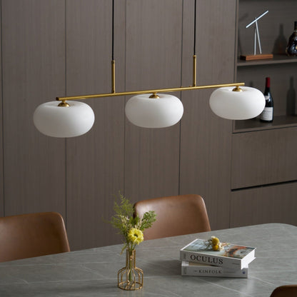 Gold-finish linear glass pendant above a dining table