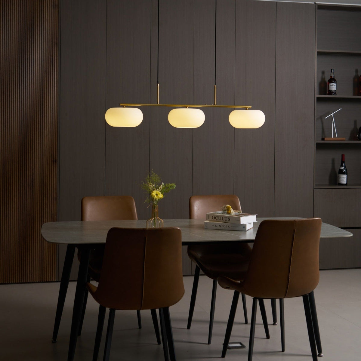Gold-finish linear glass pendant with warm light above a dining table