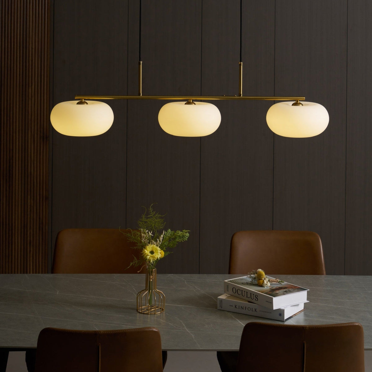 Gold-finish linear glass pendant with warm light above a dining table