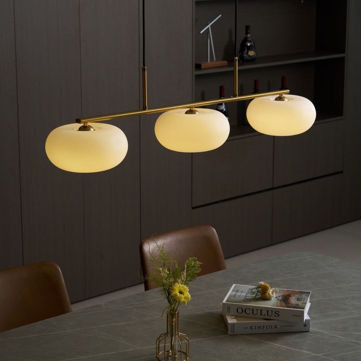 Gold-finish linear glass pendant with warm light above a dining table