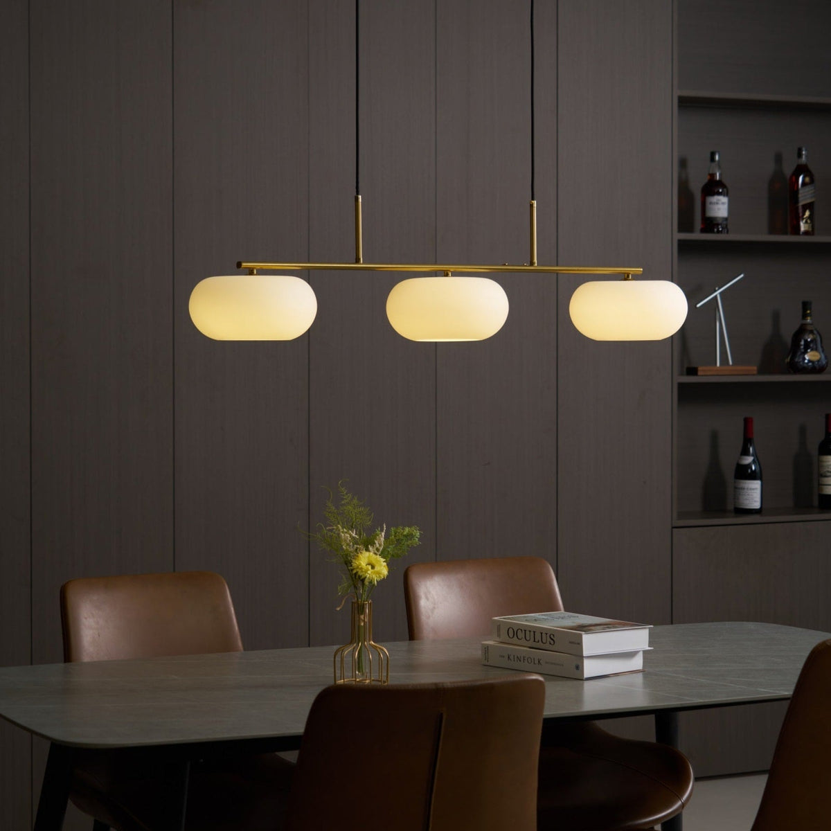 Gold-finish linear glass pendant with warm light above a dining table