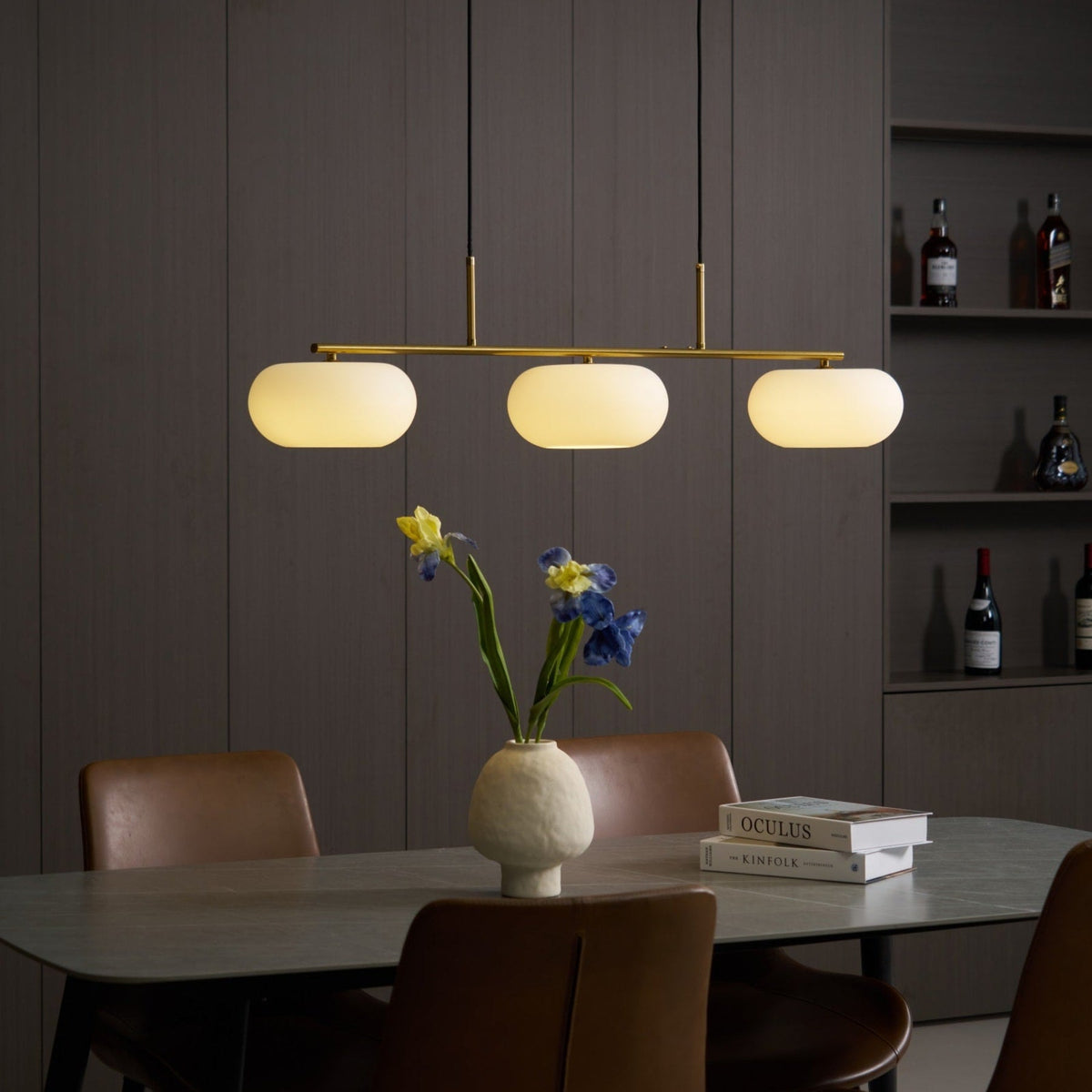 Gold-finish linear glass pendant with warm light above a dining table