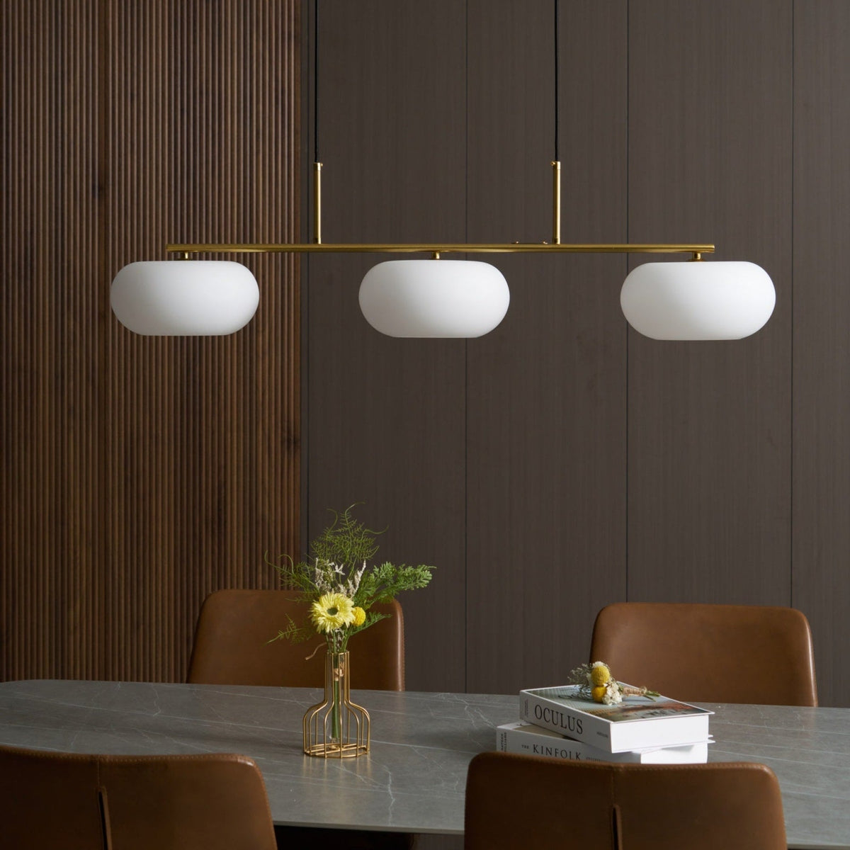 Gold-finish linear glass pendant above a dining table