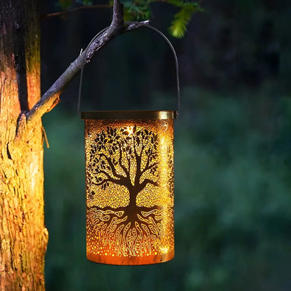 A copper-coloured Tree of Life solar lantern hanging from a tree branch, glowing with a warm light that highlights the intricate tree design.