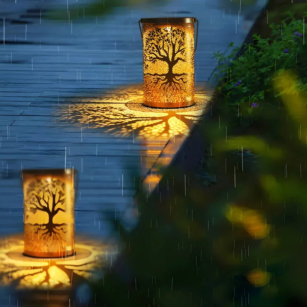 Set of two small copper Tree of Life solar lanterns casting a warm, decorative pattern onto a wet wooden garden deck in the rain.